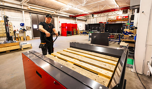 Man unloading pallets from an electric PalletMaster® dispenser with a pallet jack inside a warehouse