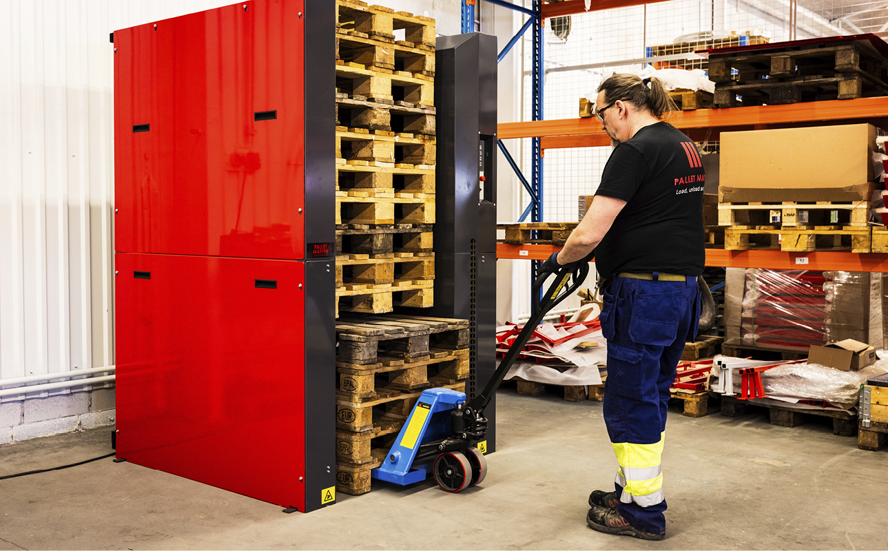 Man loading 5 new empty pallets with a pallet jack into a PalletMaster® 1-5 pallet dispenser underneath a pile of pallets