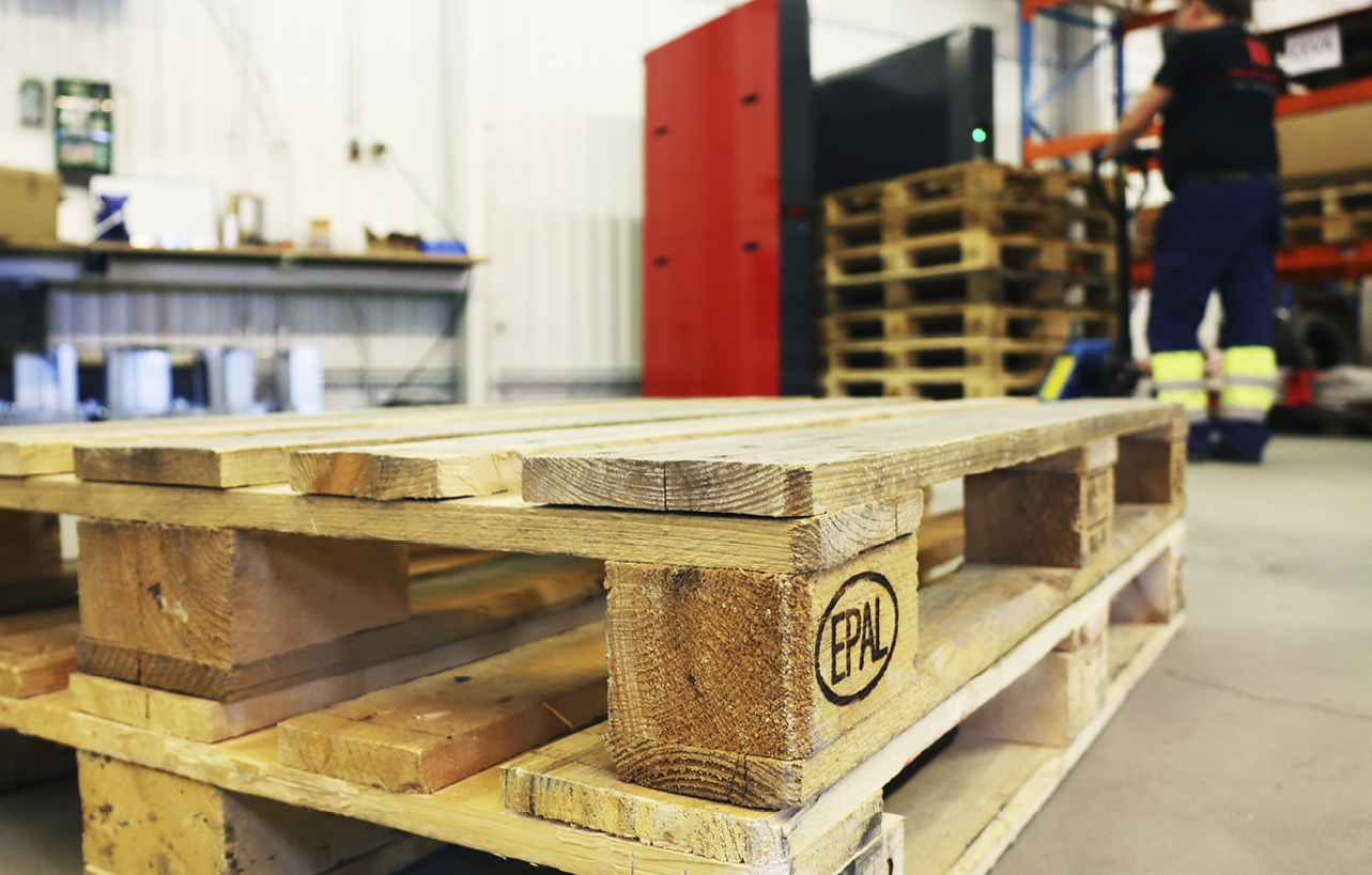Two wooden pallets on the floor waiting to be loaded into a PalletMaster® dispenser in the background
