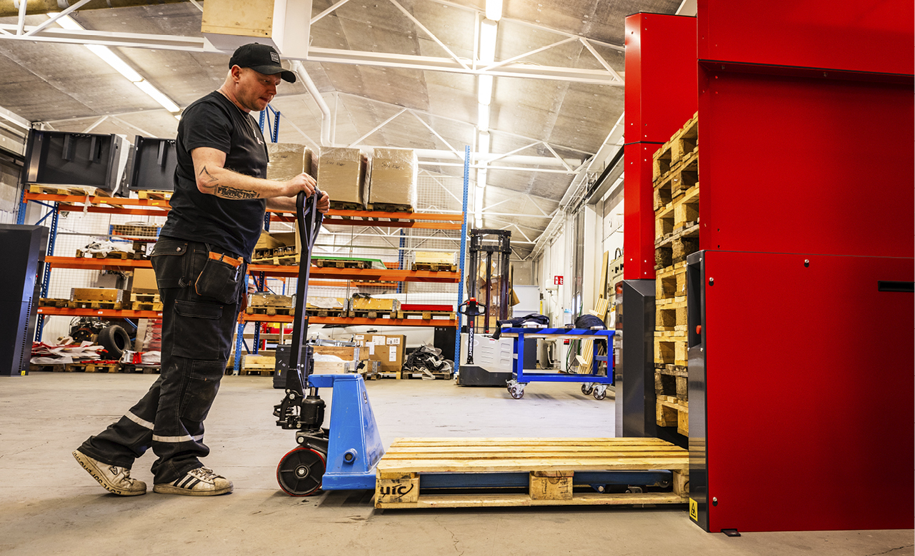 Man loading one wooden pallet into a PalletMaster® dispenser in a warehouse environment